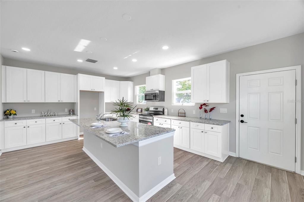 A modern kitchen features white cabinets, granite countertops, a central island, and light wood flooring — 5742 MEADOWLANE STREET, NEW PORT RICHEY, FL