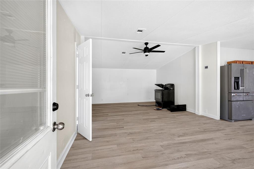 An open-concept room features light wood-look flooring, a ceiling fan, and a stainless steel refrigerator — 6766 NE 1ST PLACE, OCALA, FL