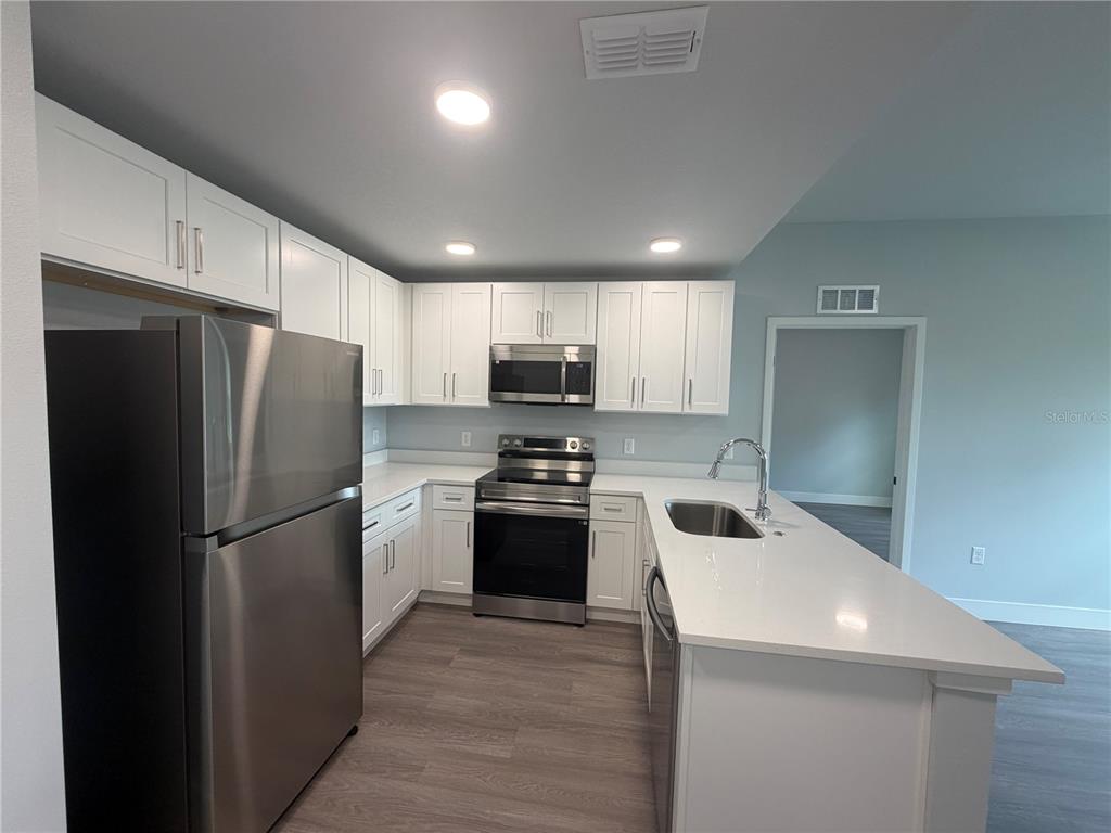 A kitchen features white cabinets, stainless steel appliances, and a white quartz countertop island — 2240 FLORIDA DRIVE UNIT 103, DELTONA, FL