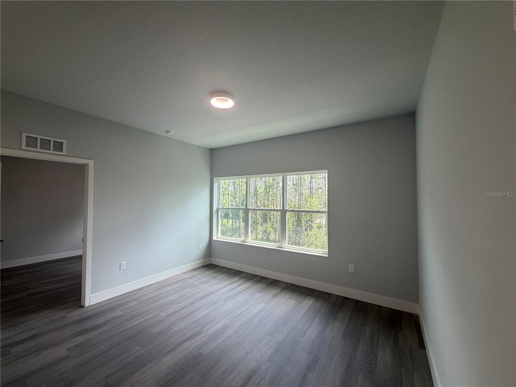 An empty room features gray walls, wood-look flooring, and a large window overlooking trees — 2240 FLORIDA DRIVE UNIT 103, DELTONA, FL