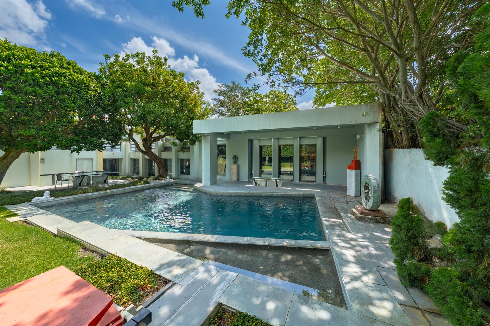 A swimming pool sits in front of a modern home with a covered patio area — 1496 N Lake Way, Palm Beach FL 33480, PALM BEACH, FL