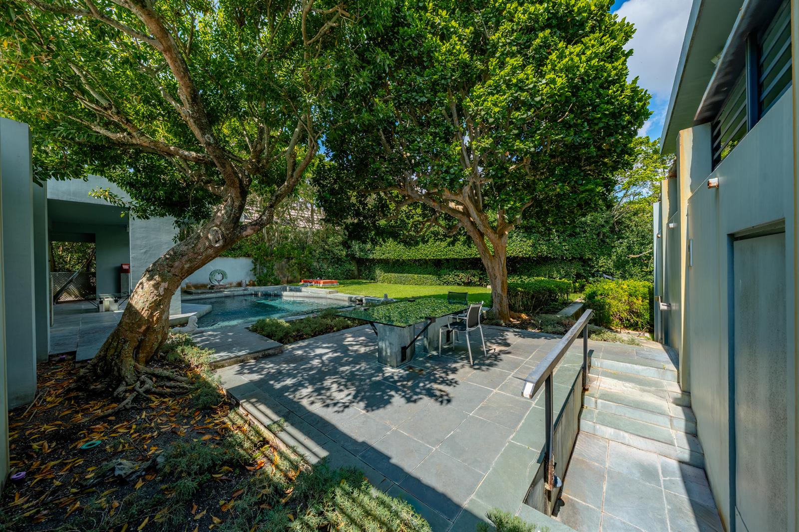 A stone patio with a glass table sits between two modern buildings and a pool — 1496 N Lake Way, Palm Beach FL 33480, PALM BEACH, FL