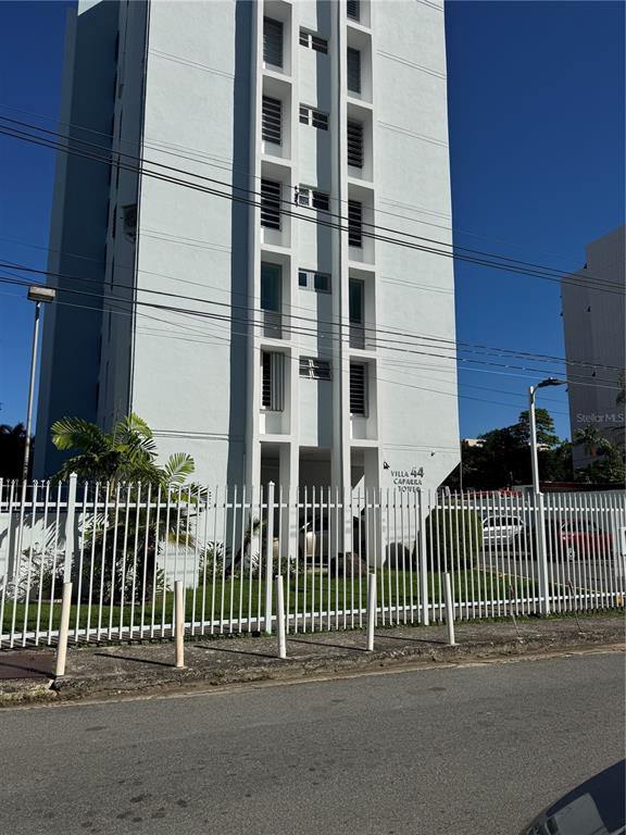 A tall, white residential apartment building stands behind a white metal fence — VILLA CAPARRA TOWER 44 A UNIT 6-A, GUAYNABO, PR
