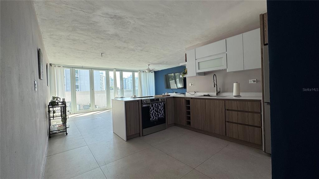 A modern kitchen with wood-tone cabinets and white upper units opens to a sunlit balcony — VILLA CAPARRA TOWER 44 A UNIT 6-A, GUAYNABO, PR