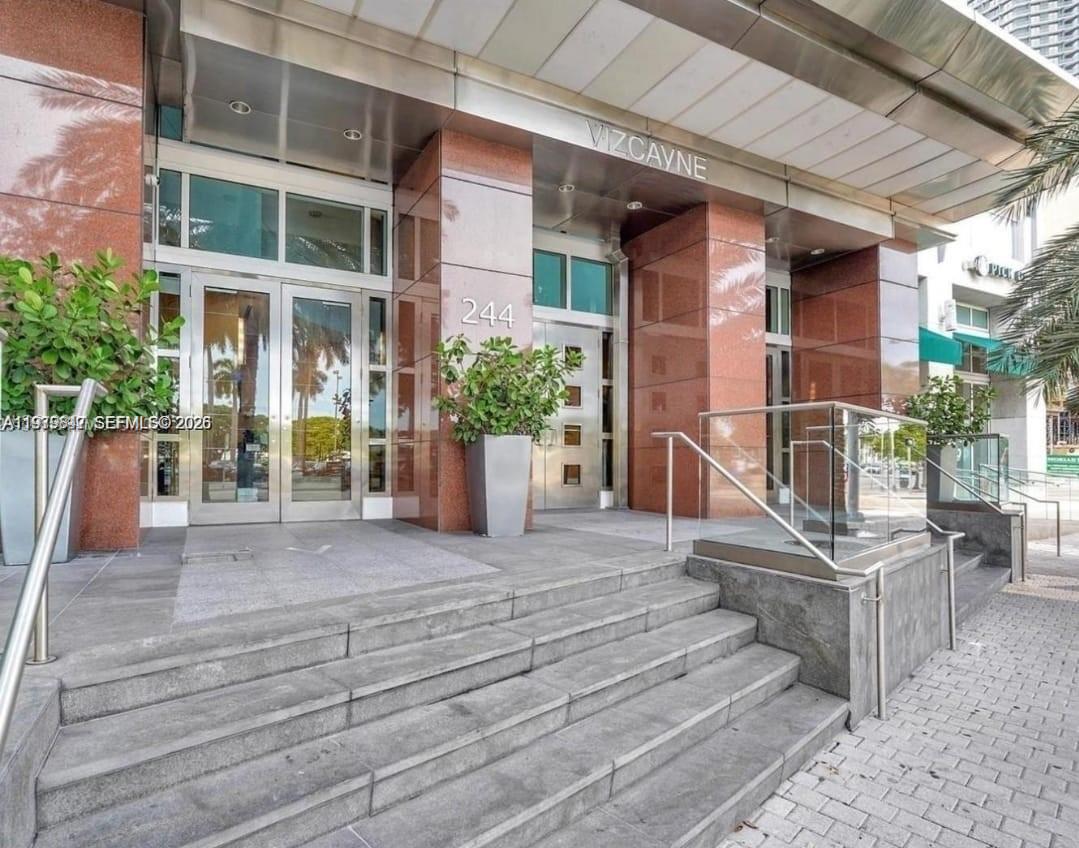 The exterior entrance of a building features stone steps, glass doors, and reddish-brown marble pillars — 244 NE Biscayne Blvd # 440, Miami FL 33132, MIAMI, FL