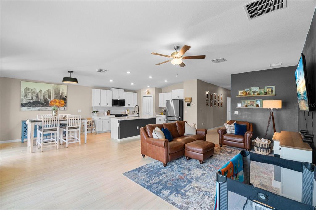 An open-concept living room and kitchen featuring light tile floors, a brown leather sofa, and white cabinetry — 13608 SUNSET SAPPHIRE COURT, PARRISH, FL