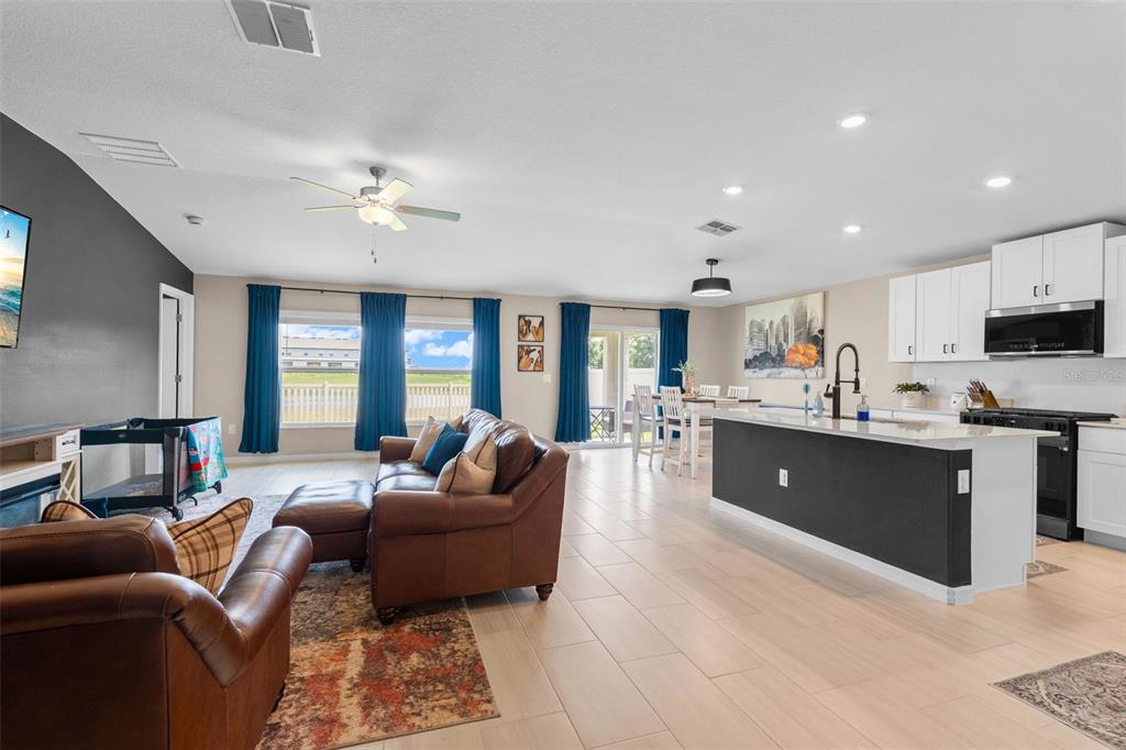 An open-concept living room and kitchen feature tile flooring, a dark island, and blue curtains — 13608 SUNSET SAPPHIRE COURT, PARRISH, FL