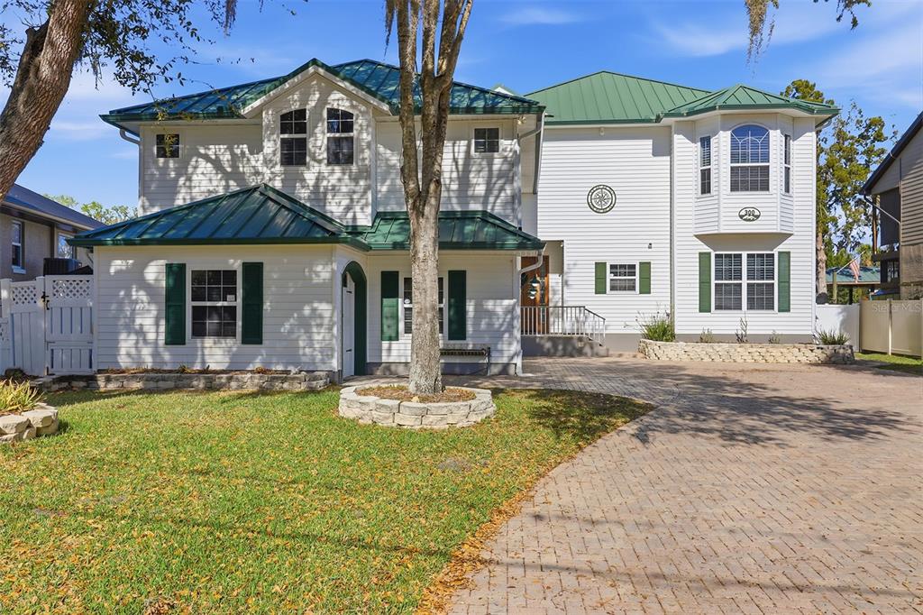 A two-story white house with a green metal roof and a brick-paved driveway — 300 NW 12TH AVENUE, CRYSTAL RIVER, FL