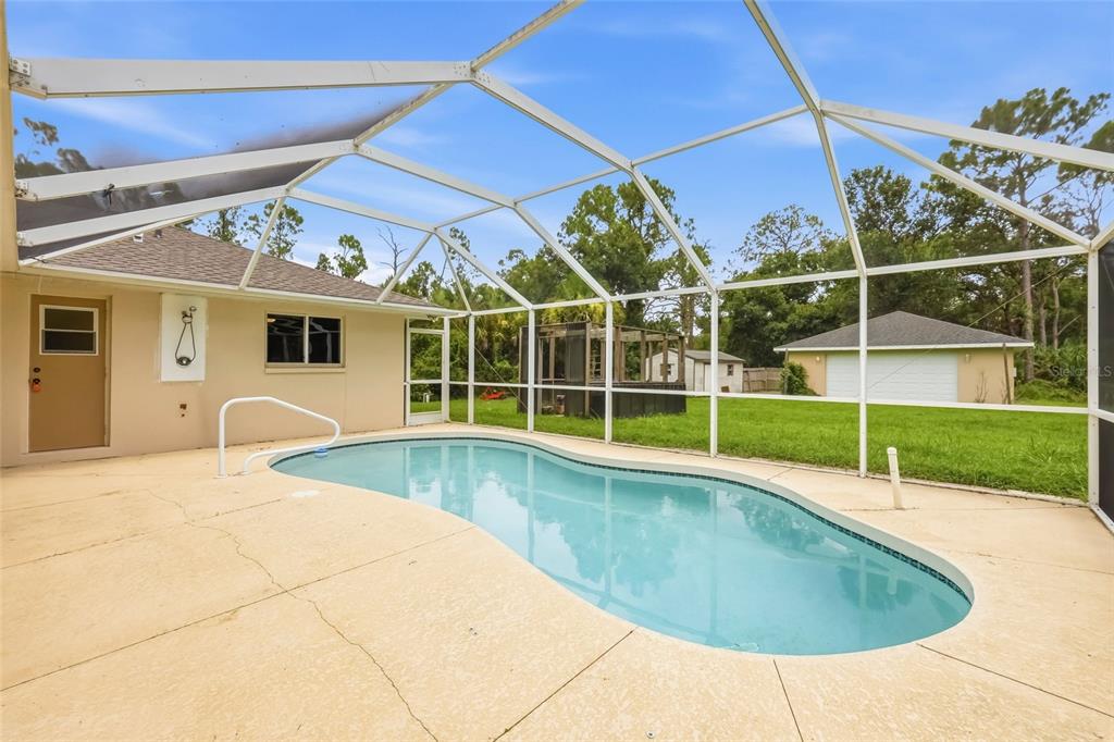 A single-story house exterior features a screened entryway, tan stucco walls, and a landscaped yard — 2209 TROPICAIRE BOULEVARD, NORTH PORT, FL