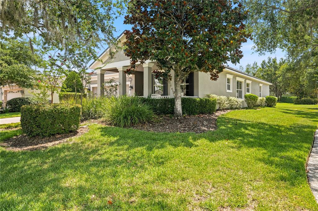 A single-story house with a covered front porch, a large magnolia tree, and manicured landscaping — 5421 CAPPLEMAN LOOP, BROOKSVILLE, FL