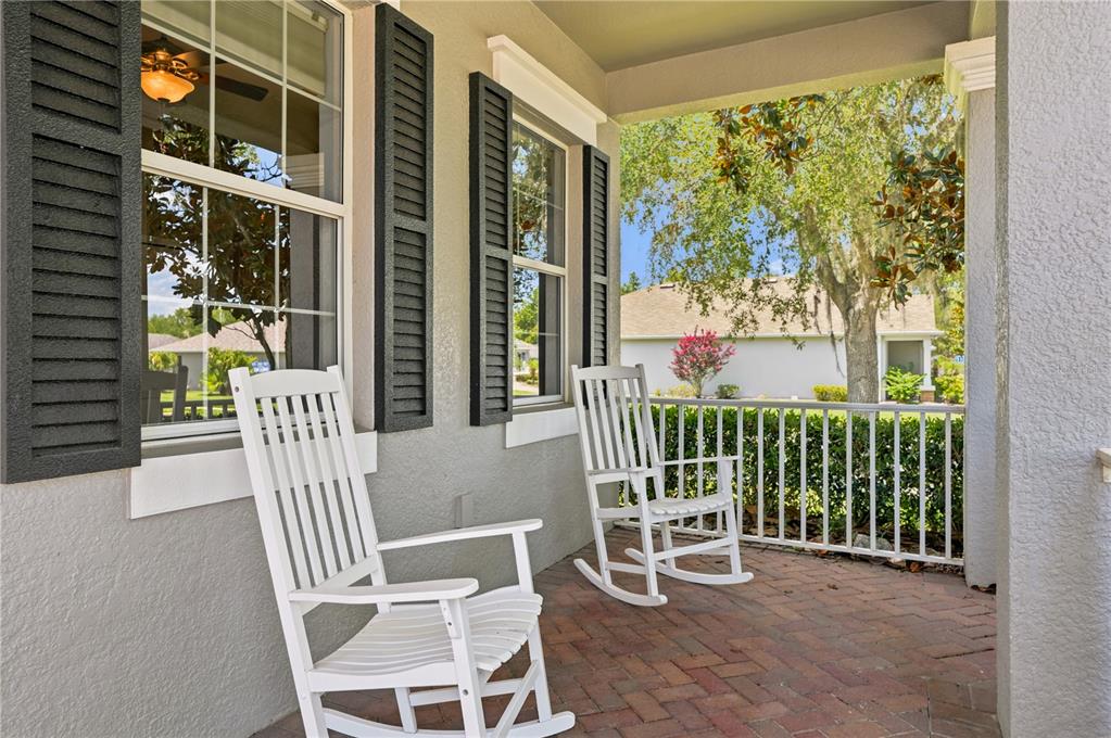 Two white rocking chairs sit on a brick-paved front porch with dark shutters and railings — 5421 CAPPLEMAN LOOP, BROOKSVILLE, FL