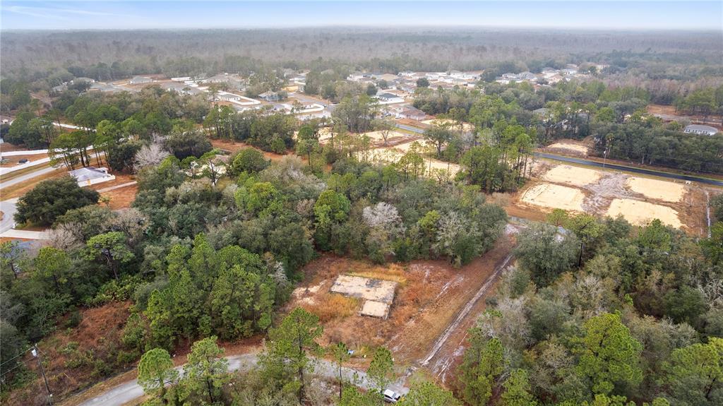 An aerial view shows a wooded lot with a concrete foundation slab and surrounding houses — 1443 TERN COURT, POINCIANA, FL