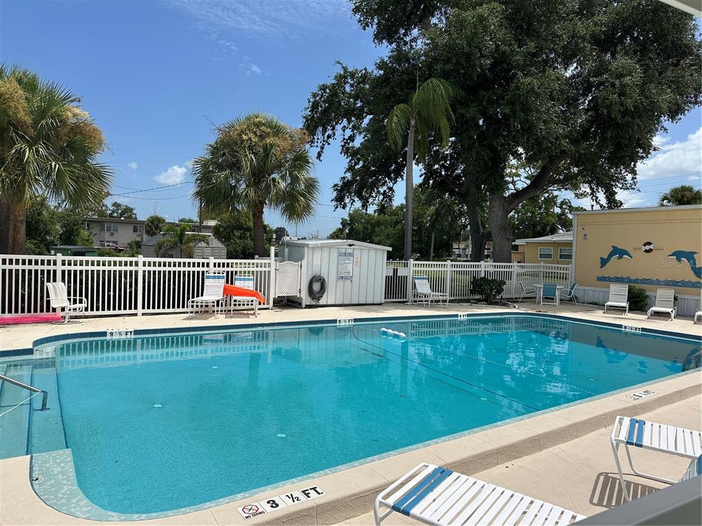 An outdoor swimming pool with lounge chairs and a white fence under a blue sky — 4150 66TH STREET N UNIT 1, ST PETERSBURG, FL