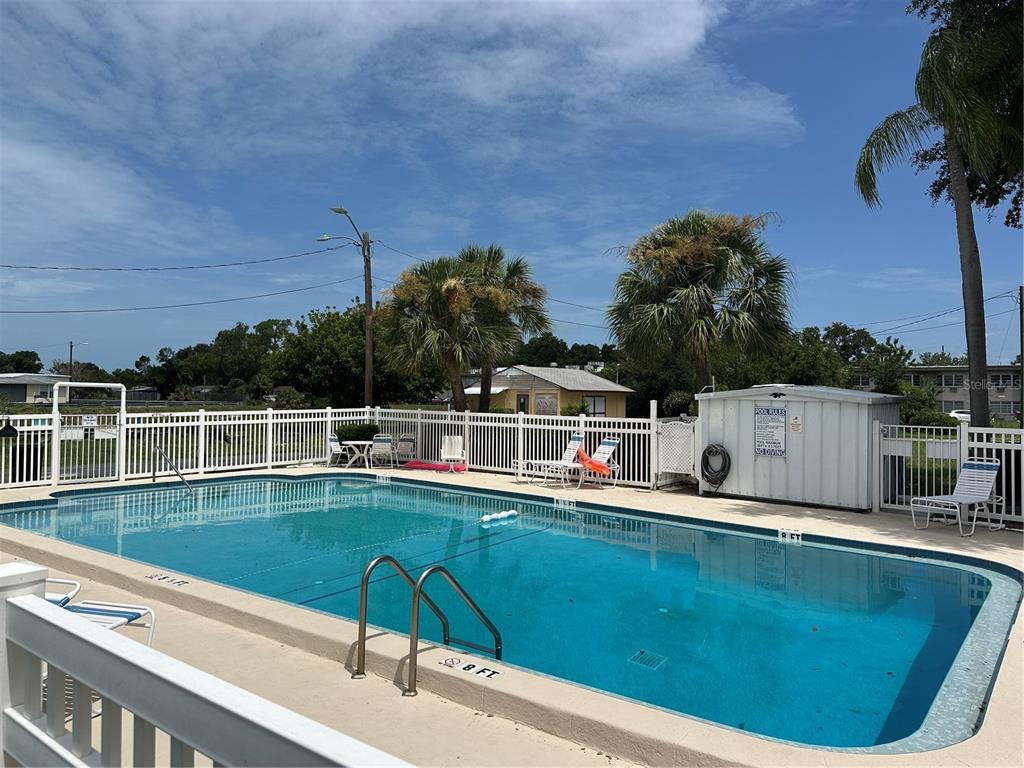 An outdoor swimming pool with a white fence and palm trees under a blue sky — 4150 66TH STREET N UNIT 1, ST PETERSBURG, FL