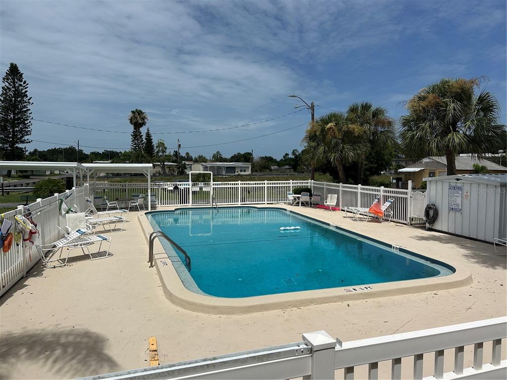 A rectangular outdoor swimming pool is surrounded by a white fence and lounge chairs — 4150 66TH STREET N UNIT 1, ST PETERSBURG, FL