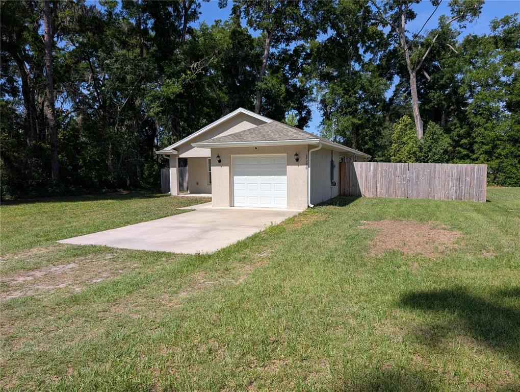 A single-story house with a white garage door and a wooden fence on a lawn — 13296 SE 33RD COURT, BELLEVIEW, FL
