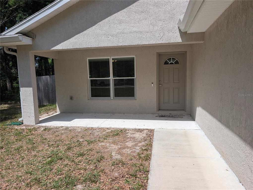 A beige stucco house exterior features a covered front porch, a window, and a door — 13296 SE 33RD COURT, BELLEVIEW, FL
