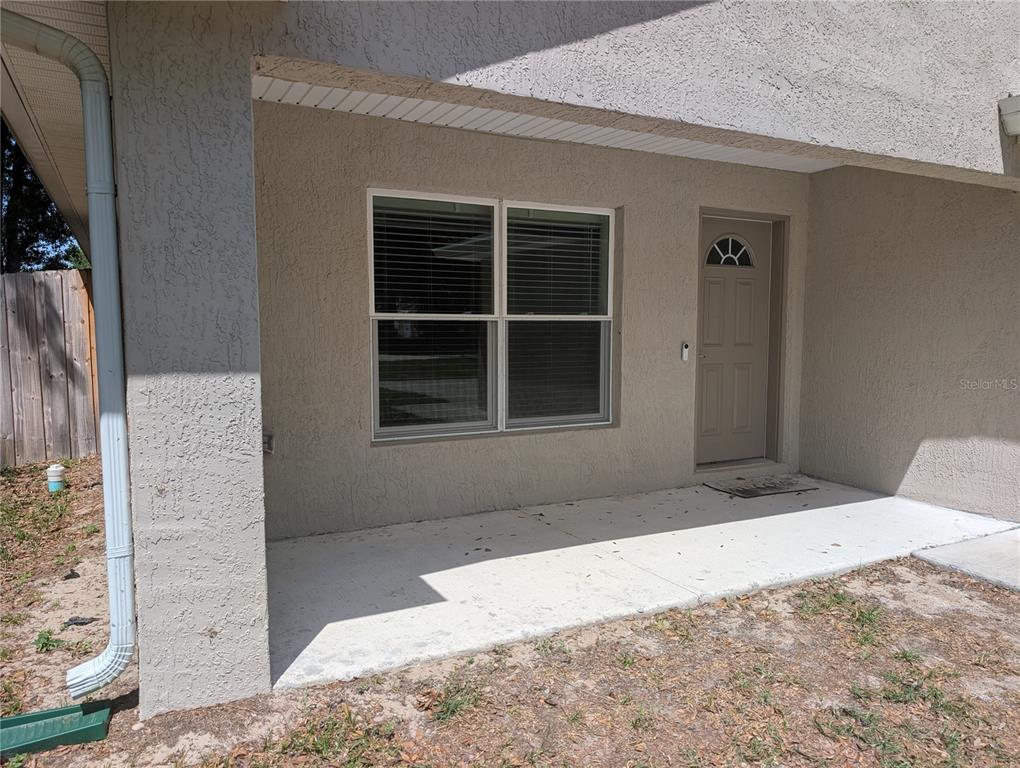 A concrete porch leads to a tan front door and a large window on a stucco home — 13296 SE 33RD COURT, BELLEVIEW, FL
