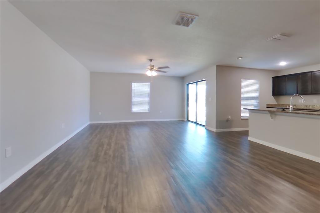 An open-concept living area features wood-look flooring, a ceiling fan, and an adjacent kitchen — 1744 CHATHAM GREEN CIRCLE, RUSKIN, FL