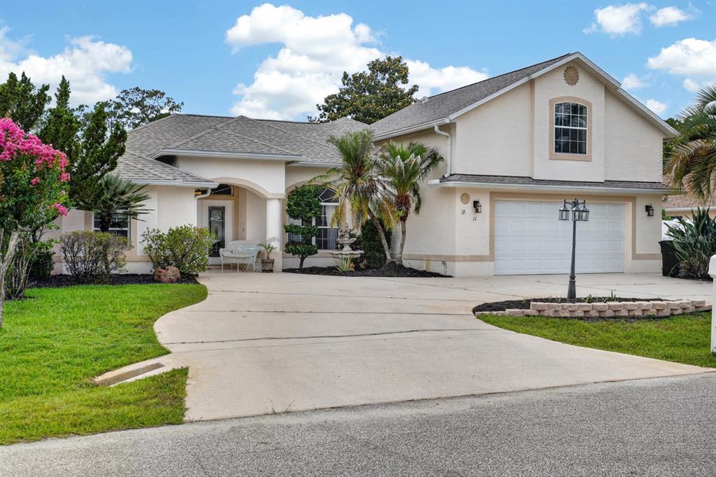 A single-story house with a beige stucco exterior, a two-car garage, and a concrete driveway — 11 ZONAL GERANIUM COURT, PALM COAST, FL