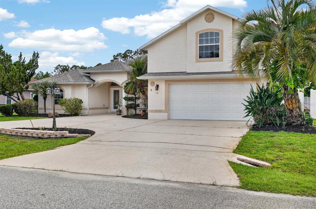 A two-story house with a beige stucco exterior, a two-car garage, and a palm tree — 11 ZONAL GERANIUM COURT, PALM COAST, FL