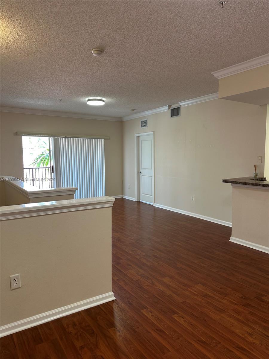 An empty living area features wood-look flooring, beige walls, and a sliding glass door — 5840 W Sample Rd # 306, Coral Springs FL 33067, CORAL SPRINGS, FL