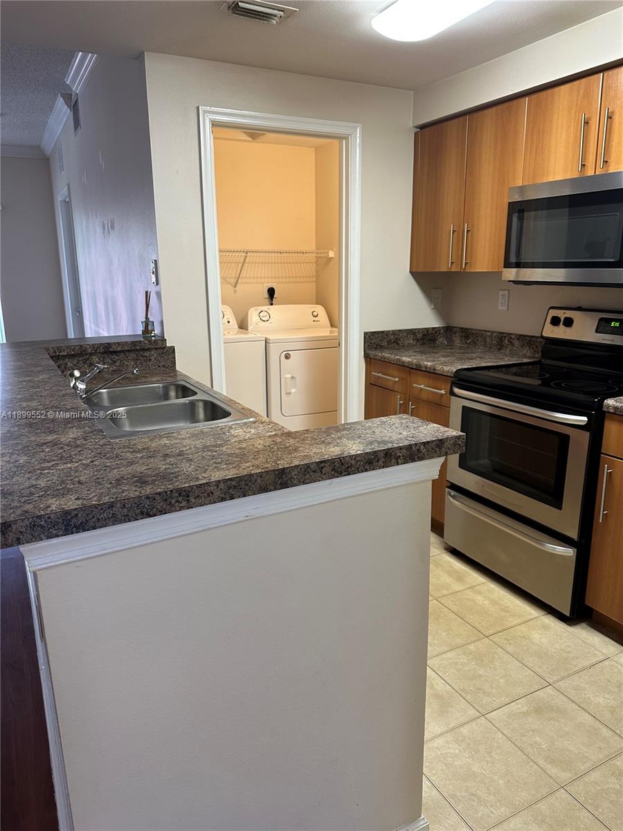 A kitchen features wood cabinets, dark laminate countertops, stainless steel appliances, and an adjacent laundry closet — 5840 W Sample Rd # 306, Coral Springs FL 33067, CORAL SPRINGS, FL
