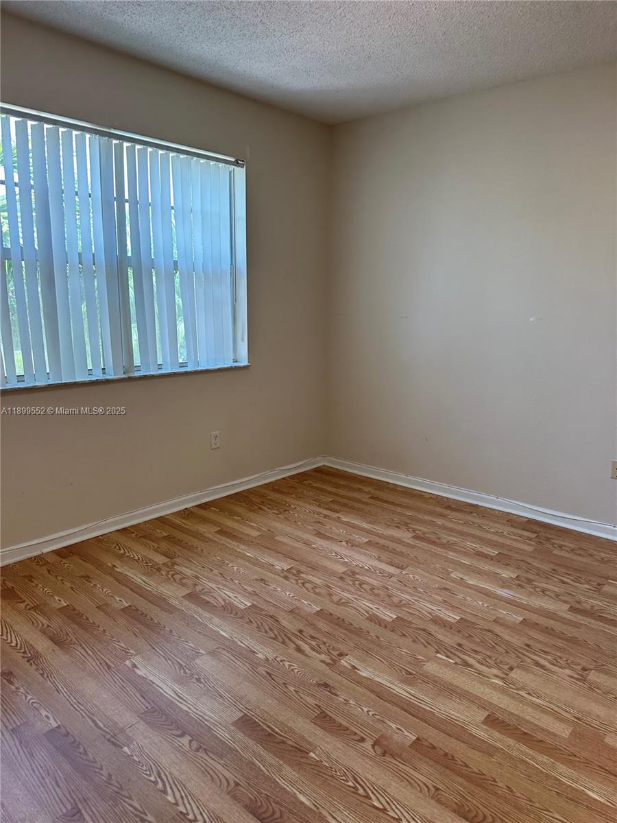 An empty room features light-colored walls, wood-look flooring, and a window with vertical blinds — 5840 W Sample Rd # 306, Coral Springs FL 33067, CORAL SPRINGS, FL