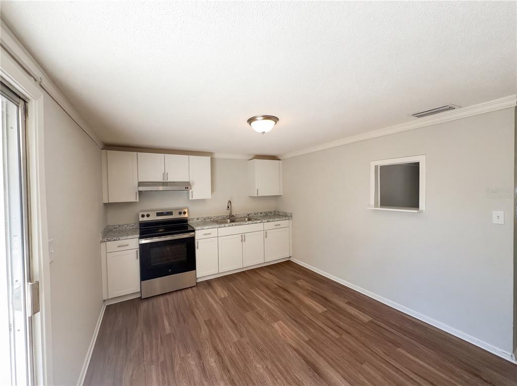 A kitchen features white cabinets, stainless steel appliances, granite countertops, and wood-look flooring — 1830 BELLGROVE STREET, LAKELAND, FL
