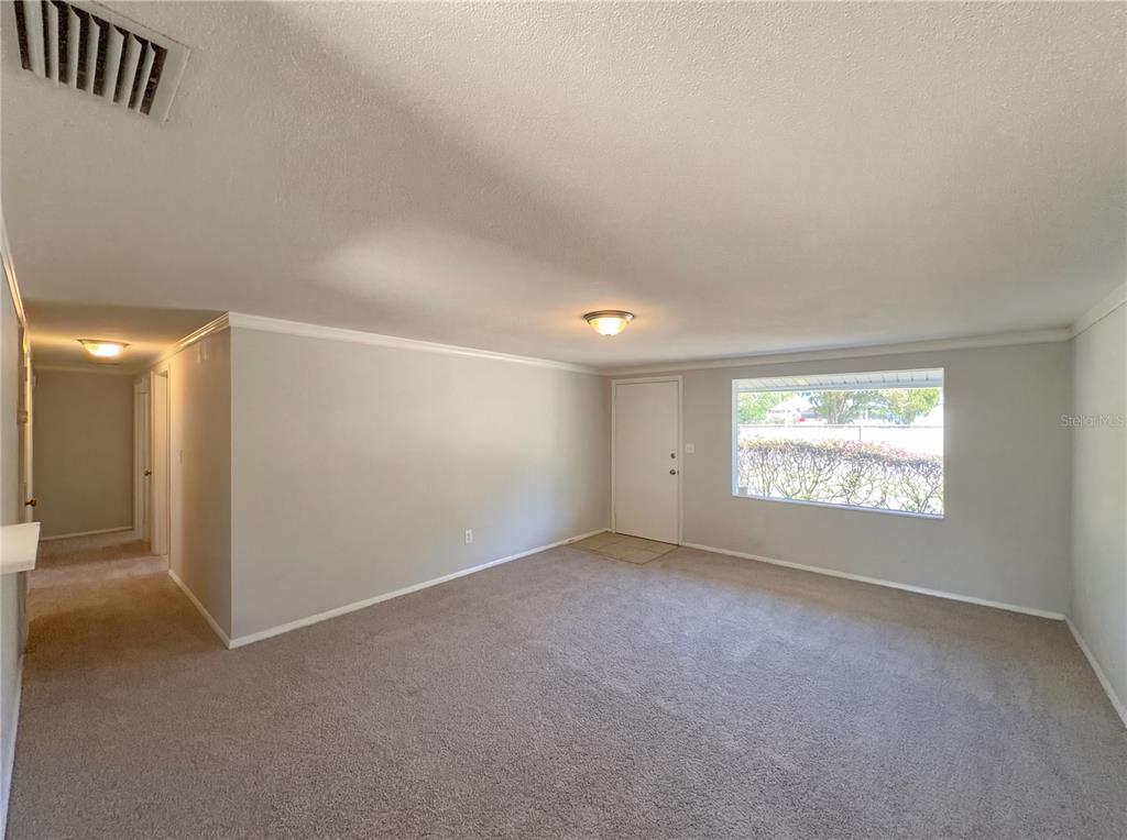 A carpeted living room features light gray walls, a ceiling light, and a front door — 1830 BELLGROVE STREET, LAKELAND, FL