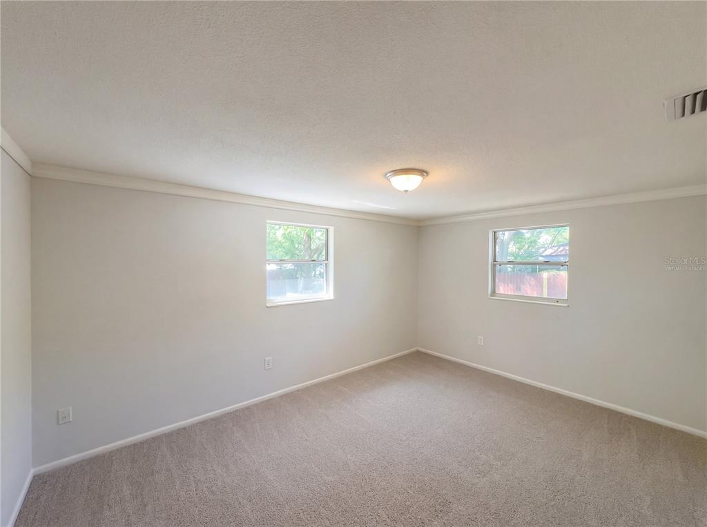 An empty bedroom with beige carpet, light-colored walls, two windows, and a ceiling light fixture — 1830 BELLGROVE STREET, LAKELAND, FL