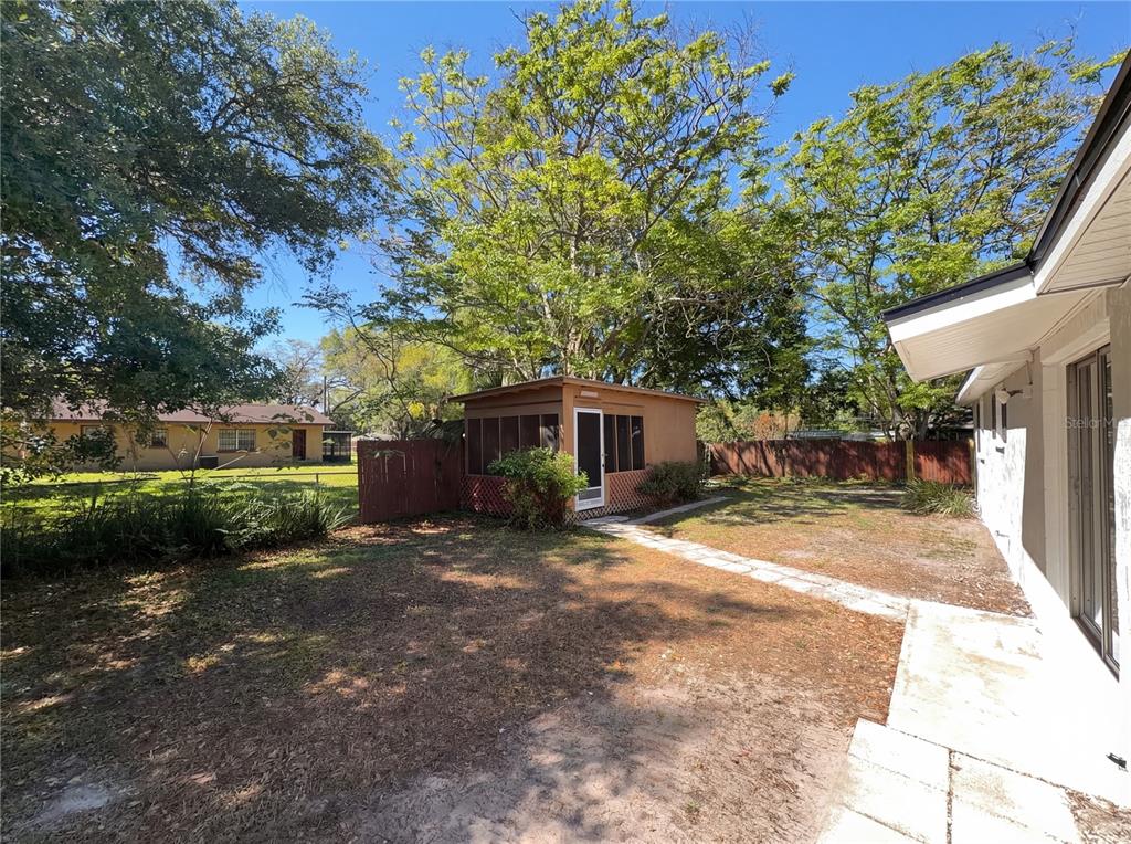 A backyard view featuring a small screened-in structure, a stone path, and mature trees — 1830 BELLGROVE STREET, LAKELAND, FL