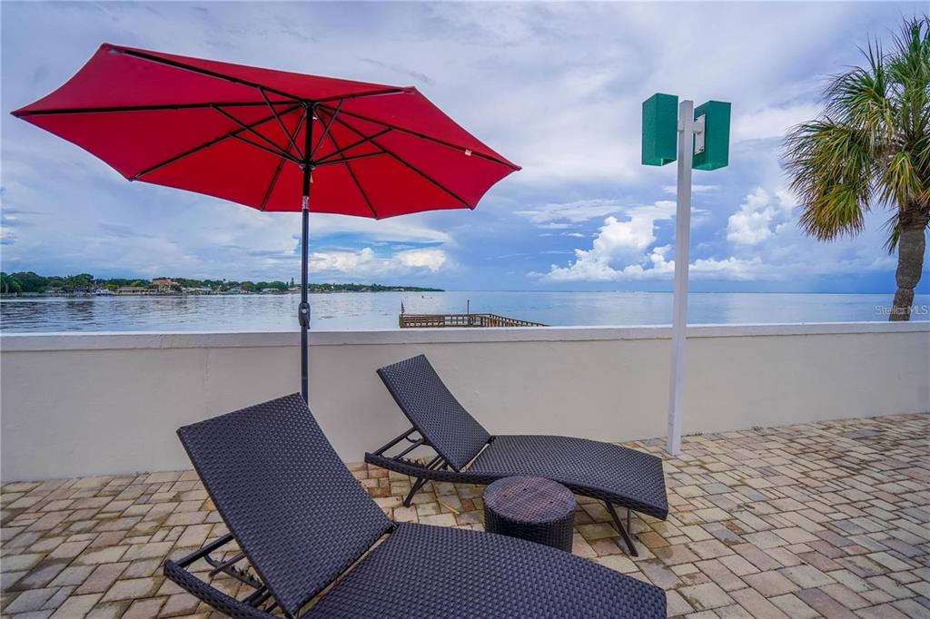 Two lounge chairs and a red umbrella sit on a paved patio overlooking the water — 7100 SUNSHINE SKYWAY LANE S UNIT 201, ST PETERSBURG, FL