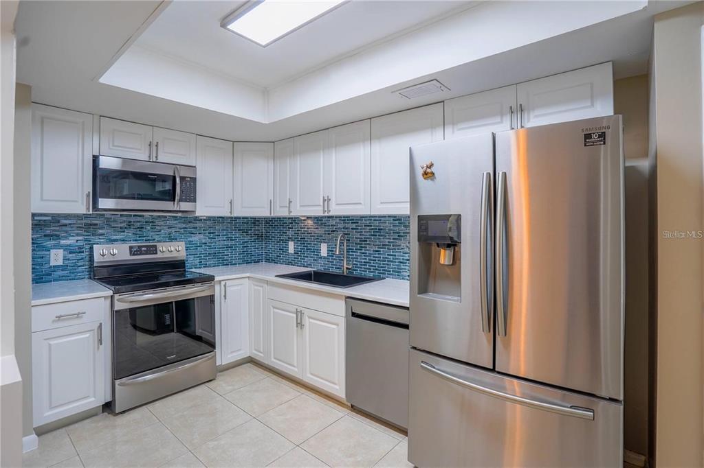 A kitchen with white cabinets, stainless steel appliances, and a blue glass tile backsplash — 7100 SUNSHINE SKYWAY LANE S UNIT 201, ST PETERSBURG, FL