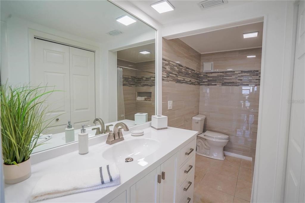 A bathroom features a white vanity with a sink, a large mirror, and a toilet — 7100 SUNSHINE SKYWAY LANE S UNIT 201, ST PETERSBURG, FL