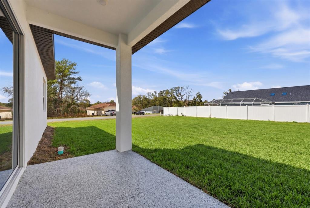 A covered concrete patio overlooks a grassy backyard enclosed by a white vinyl fence — 4487 SW 152 STREET, OCALA, FL