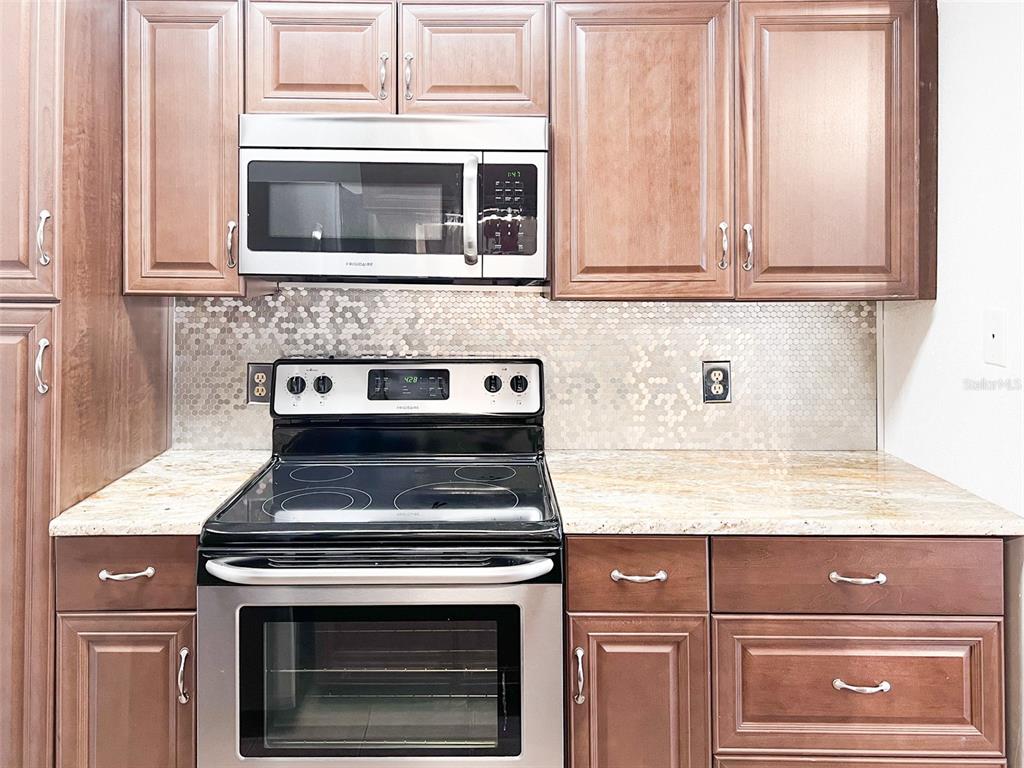 A kitchen features wood cabinets, stainless steel appliances, granite countertops, and a circular tile backsplash — 11901 4TH STREET N UNIT 8102, ST PETERSBURG, FL
