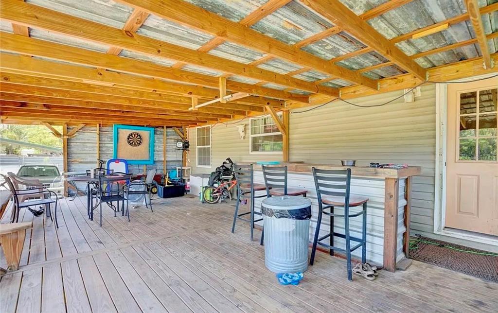 A covered wooden deck features a bar area, outdoor seating, and a corrugated metal roof — 201 E MAXANNA, SEBRING, FL
