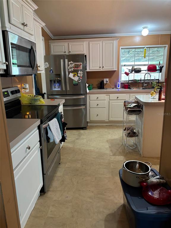 A kitchen features white cabinetry, stainless steel appliances, and a light-colored tile floor — 201 E MAXANNA, SEBRING, FL
