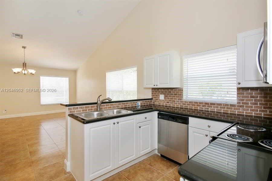 A kitchen features white cabinets, a stainless steel dishwasher, and a brown brick backsplash — BOCA RATON, FL