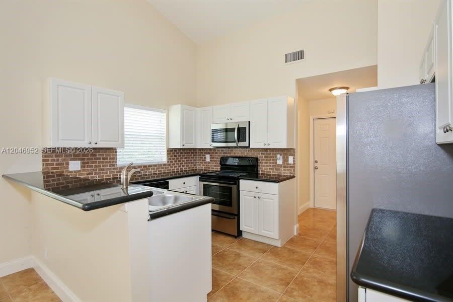 A kitchen features white cabinets, black countertops, stainless steel appliances, and a brick backsplash — BOCA RATON, FL