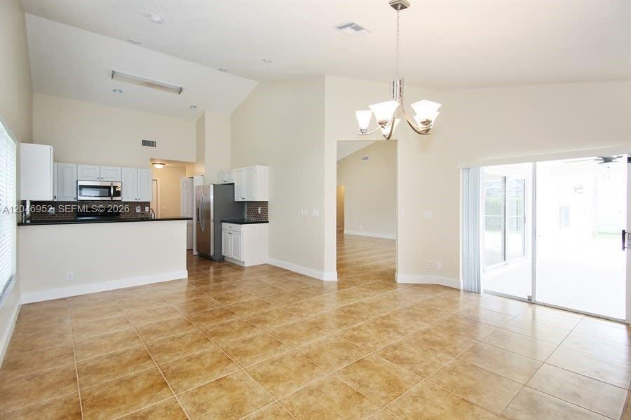 A kitchen with white cabinets and tile flooring opens into a spacious living area — BOCA RATON, FL
