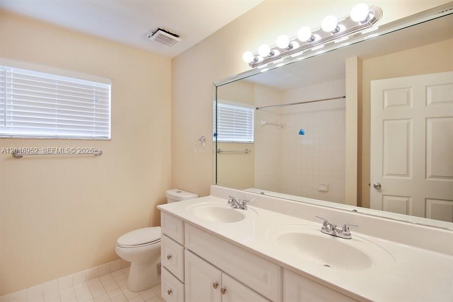 A bathroom features a double vanity with white cabinets, a large mirror, and a toilet — BOCA RATON, FL