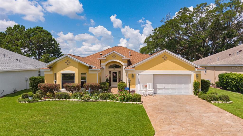 A yellow single-story house with a brown shingled roof and a paved driveway — 16840 SE 85TH SAPELO COURT, THE VILLAGES, FL