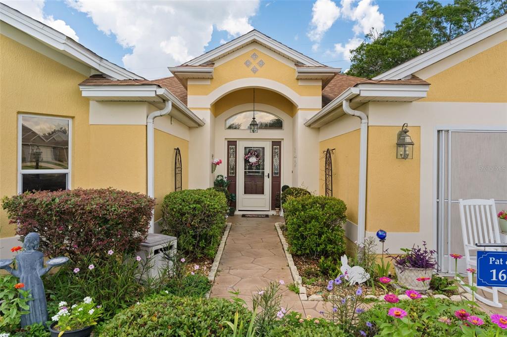 The exterior of a yellow house features a stone walkway leading to the front door — 16840 SE 85TH SAPELO COURT, THE VILLAGES, FL