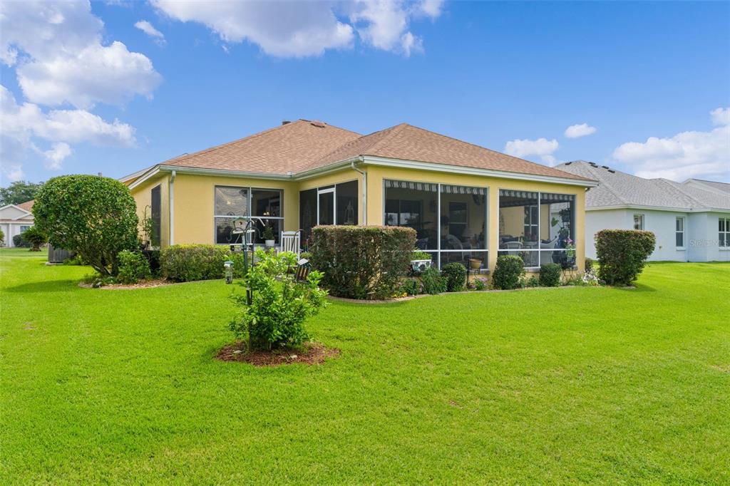 The backyard of a yellow house features a screened-in porch and a large lawn — 16840 SE 85TH SAPELO COURT, THE VILLAGES, FL