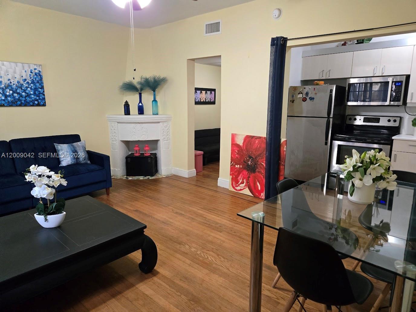 A living room with a fireplace and blue sofa connects to a kitchen with stainless appliances — 1219 Meridian Ave # 2, Miami Beach FL 33139, MIAMI BEACH, FL