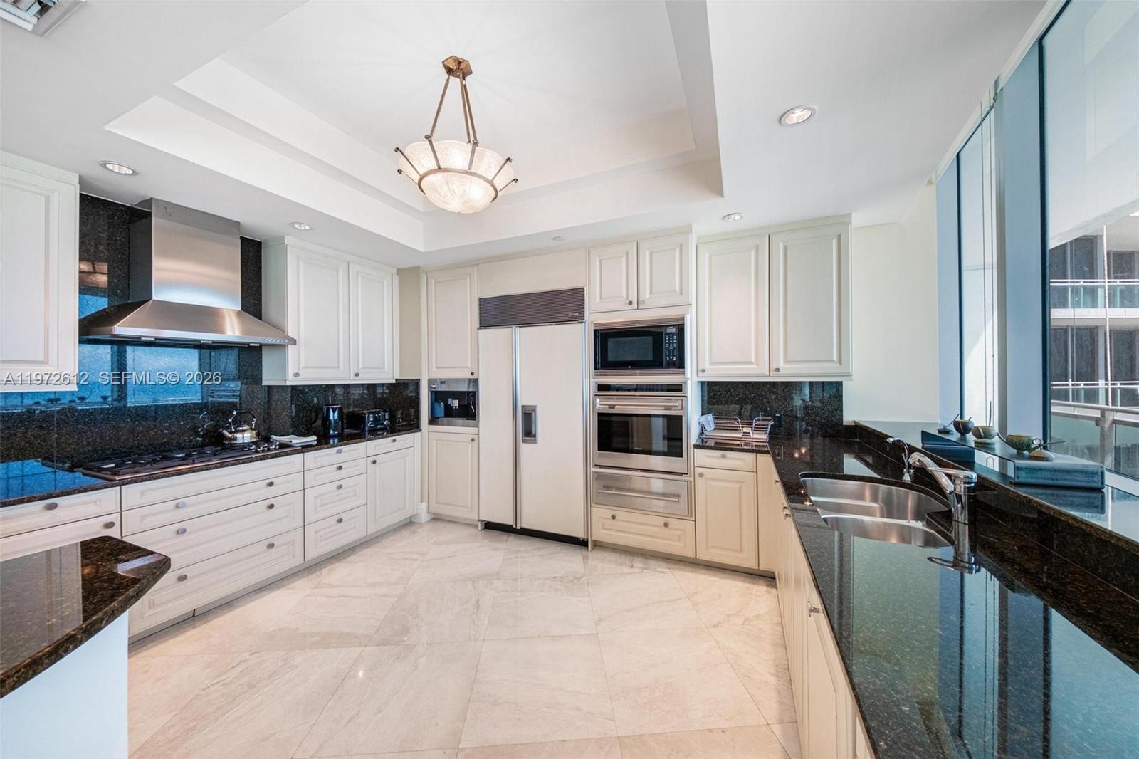 A kitchen features white cabinetry, dark granite countertops, stainless steel appliances, and light tile flooring — 10295 Collins Ave # 1502, Bal Harbour FL 33154, BAL HARBOUR, FL