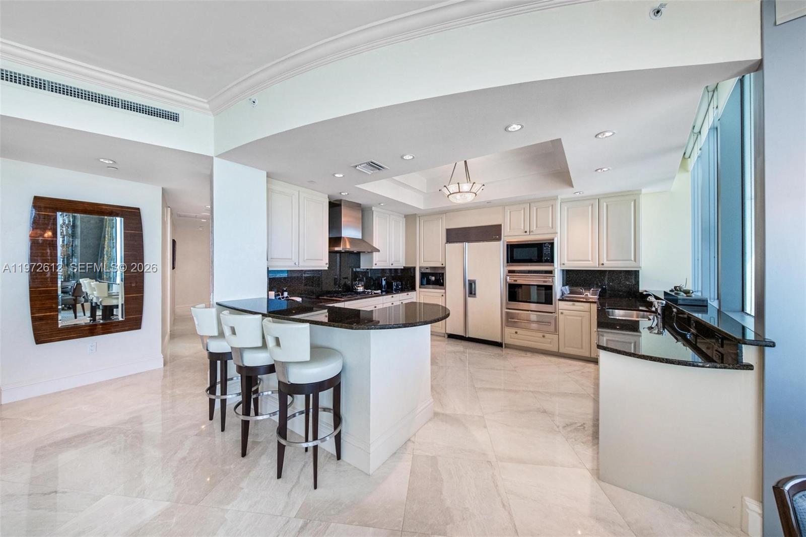 A modern kitchen features white cabinetry, granite countertops, a breakfast bar, and marble flooring — 10295 Collins Ave # 1502, Bal Harbour FL 33154, BAL HARBOUR, FL