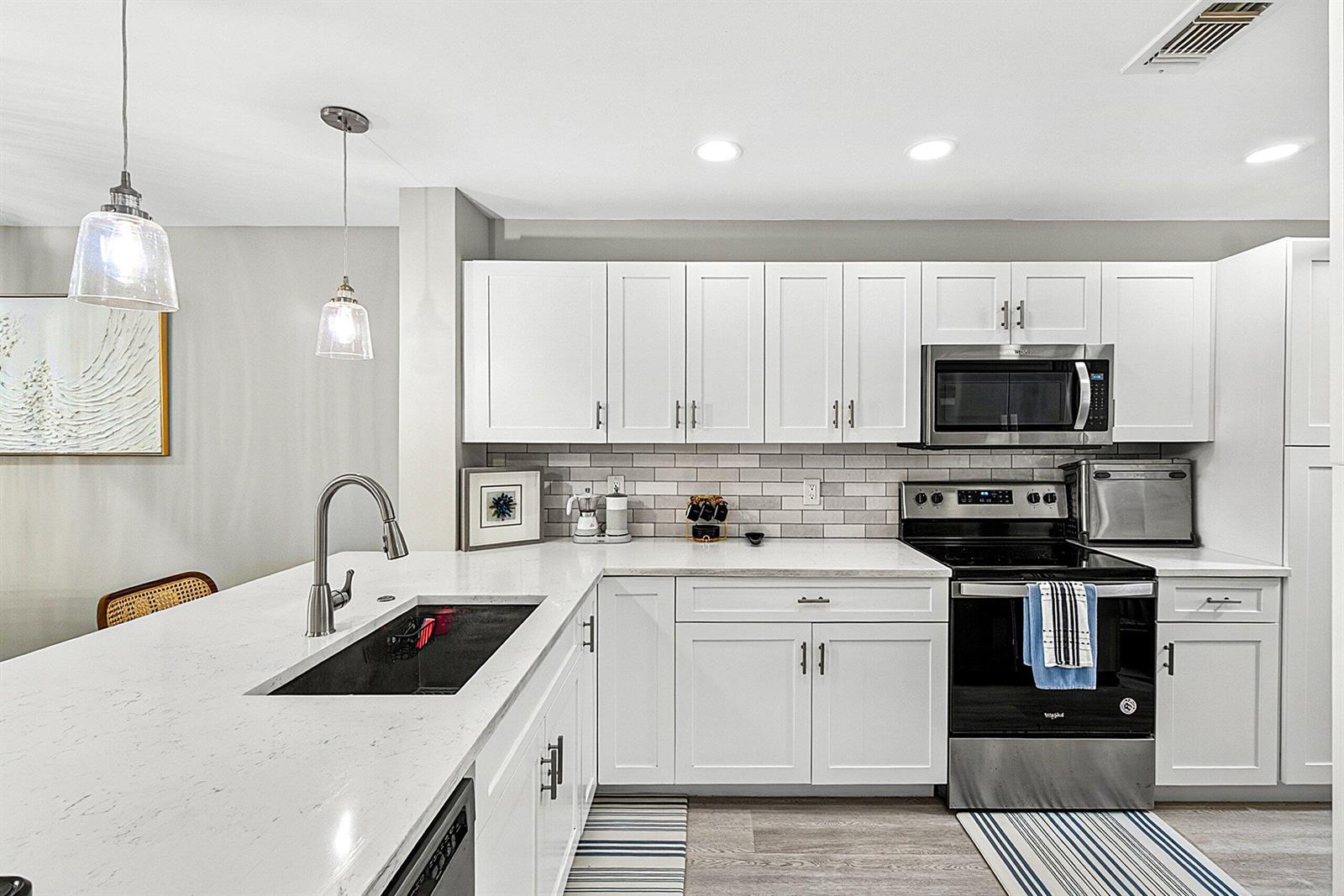 A modern kitchen features white cabinets, a quartz countertop, a black sink, and stainless appliances — 35 Southport Lane # D, Boynton Beach FL 33436, BOYNTON BEACH, FL